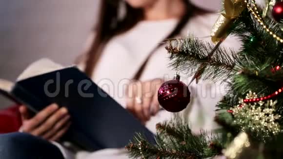 美丽的年轻女士坐在圣诞树附近的椅子上看书视频的预览图
