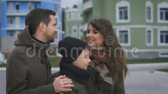 幸福的年轻家庭穿着温暖的衣服站在街上微笑爸爸和妈妈在笑视频的预览图