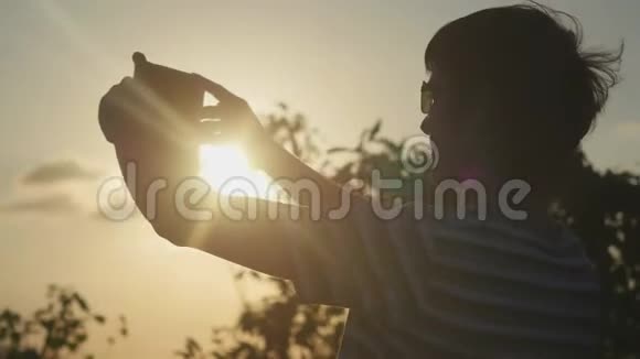 年轻的游客戴着太阳镜在山顶拍摄日落3840x2160视频的预览图