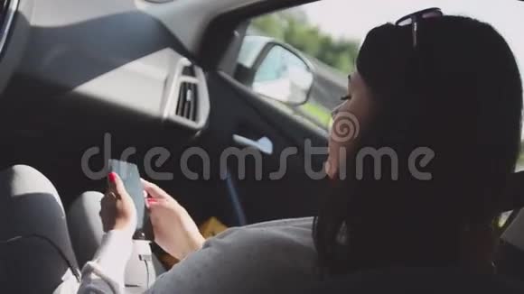 年轻的黑发女孩坐在驾驶汽车的乘客座位上打电话夏日晴天视频的预览图
