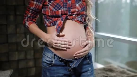 一位美丽的孕妇站在窗户附近用婴儿摸着她美妙的肚子青年视频的预览图