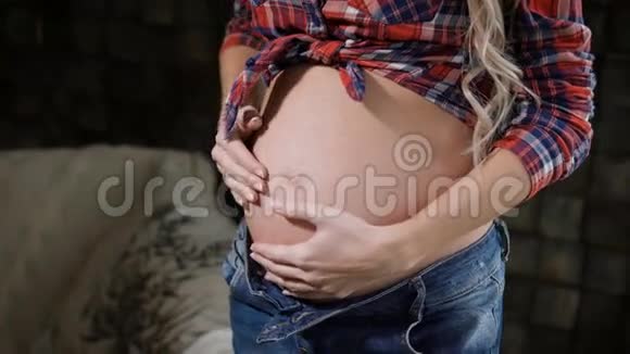 一个穿着蓝色牛仔裤和格子衬衫的快乐年轻孕妇迷人的腹部和手的特写美丽的未来视频的预览图