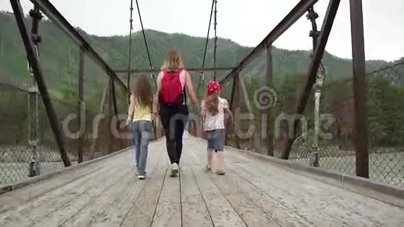 妈妈和女儿正在雨中沿着桥走一家人在山里旅行年轻女游客视频的预览图