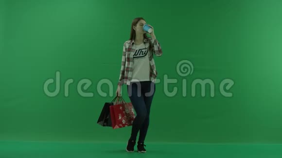 女孩站在绿色的屏幕上拿着袋子喝着杯子里的东西视频的预览图