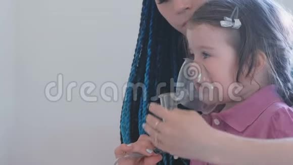 女孩用她妈妈的口罩吸入使用雾化器和吸入器进行治疗视频的预览图
