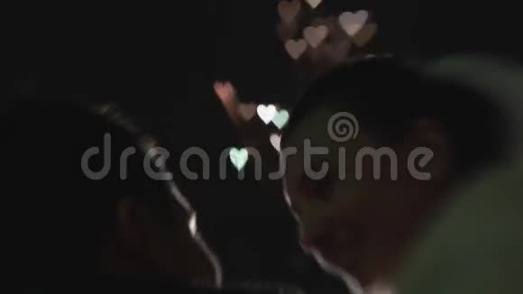 在亲吻新婚夫妇的背后烟花在夜空中以五彩缤纷的心的形式爆炸视频的预览图