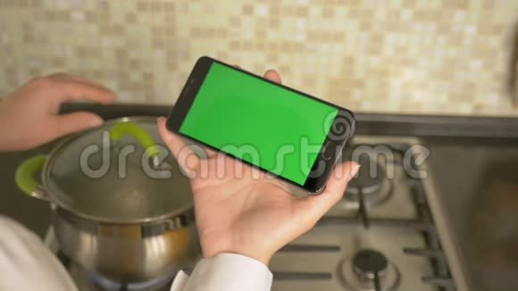 一个女人拿着一台绿色屏幕的智能手机煮汤视频的预览图
