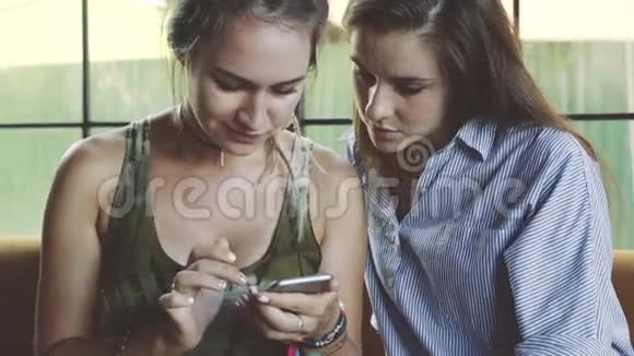 两个情绪化的女性朋友在咖啡馆里使用智能手机视频的预览图