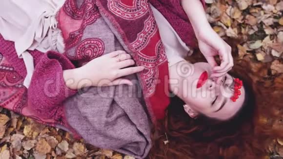 美丽的红发女孩的俯视图躺在干燥的叶子上在秋天的森林中缓慢地放松3840x2160视频的预览图