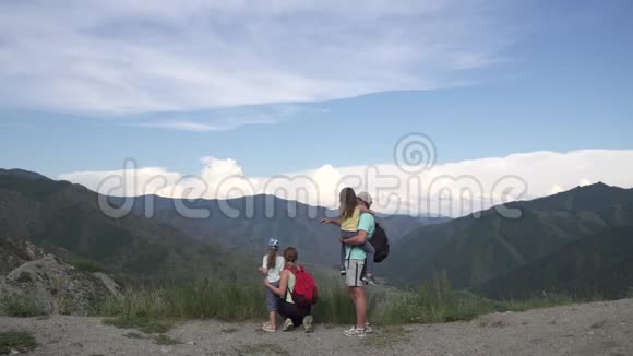 父母和他们的孩子去山区旅行父亲和母亲牵着小女儿的手给她们看视频的预览图