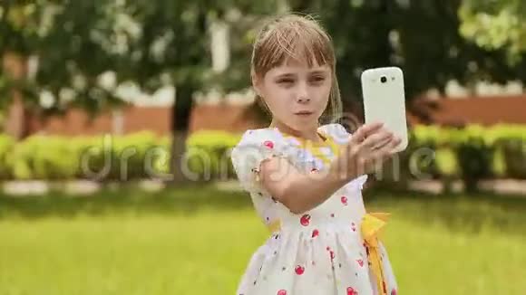 穿着白色连衣裙的小女孩在草地上自拍视频的预览图