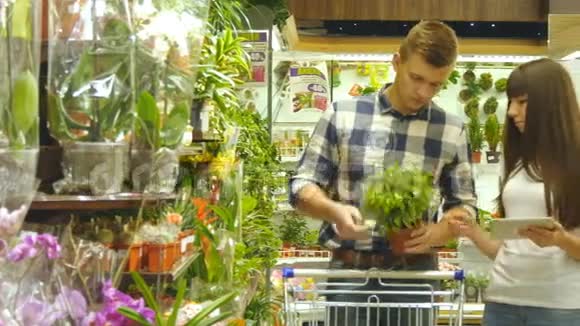 年轻漂亮的夫妇带着超市手推车在购物中心选择室内植物人在接受视频的预览图