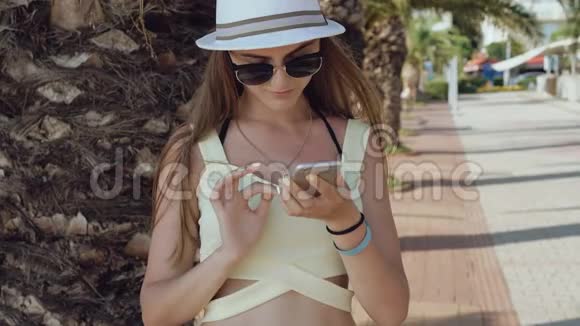 在炎热的夏天时尚女孩在街上使用手机视频的预览图