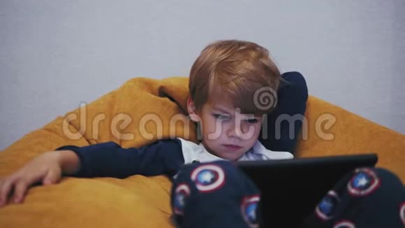 坐在沙发上看平板电脑的男孩视频的预览图