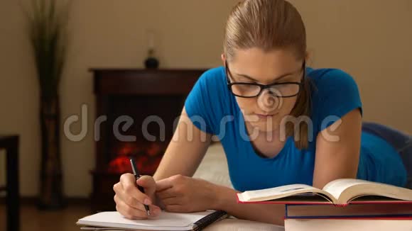 漂亮的大学生戴着眼镜躺在沙发上学习在笔记本上做笔记视频的预览图