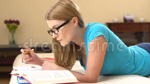 漂亮的大学生戴着眼镜躺在沙发上学习在笔记本上做笔记视频的预览图