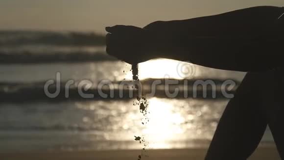 年轻女子玩沙子的手臂日落时分一只雌手用手指在大海上撒着海沙视频的预览图