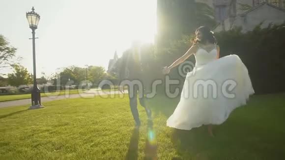 幸福的新郎新娘牵着双手在阳光下的绿草上奔跑视频的预览图