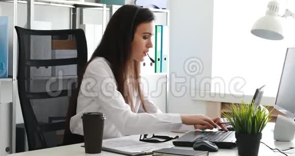 女人在耳机上说话在现代办公室里使用笔记本电脑视频的预览图