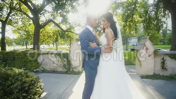 快乐的新娘和新郎在绿色公园的小巷中间接吻视频的预览图