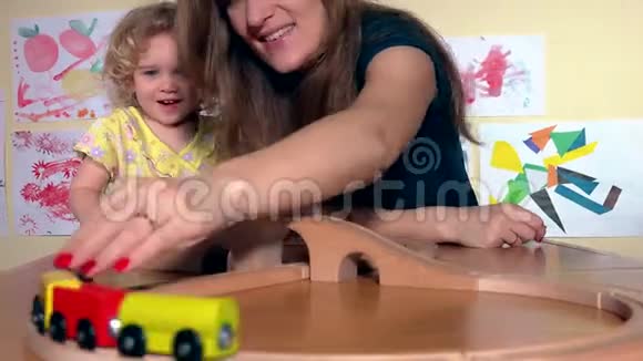 快乐的保姆和幼儿女孩在幼儿园玩木火车视频的预览图