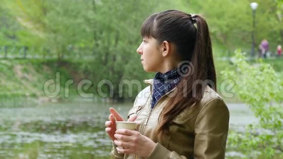 美丽的年轻女孩在公园里喝着一次性杯子里的外卖咖啡有魅力的妇女肖像视频的预览图