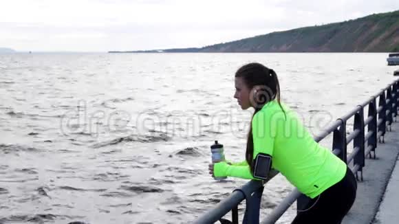运动女子海上看在城市堤岸上休息手持一瓶水视频的预览图