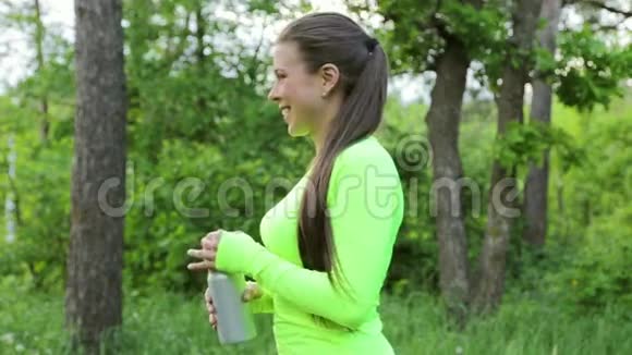 女人在森林里运动后喝水然后看镜头微笑视频的预览图