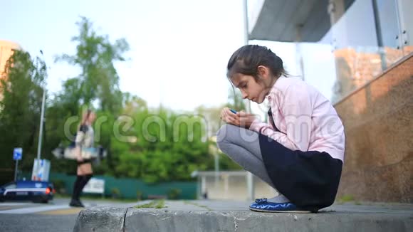 悲伤的女学生坐在街上看着她的电话等待一个电话视频的预览图
