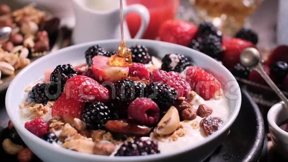 慢动作视角早餐用干水果将蜂蜜倒入一碗麦片和浆果中视频的预览图
