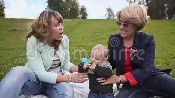 在自然界快乐妈妈奶奶亲吻她的孩子带着玩具在草地上的孩子视频的预览图