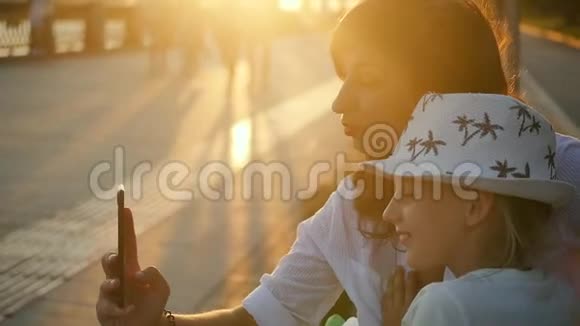 迷人的妈妈和可爱的小女儿在日落时在公园玩和自拍视频的预览图