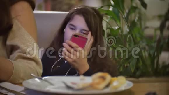 坐在快餐店里听智能手机音乐的少女女婴在室内的咖啡馆里吃披萨视频的预览图