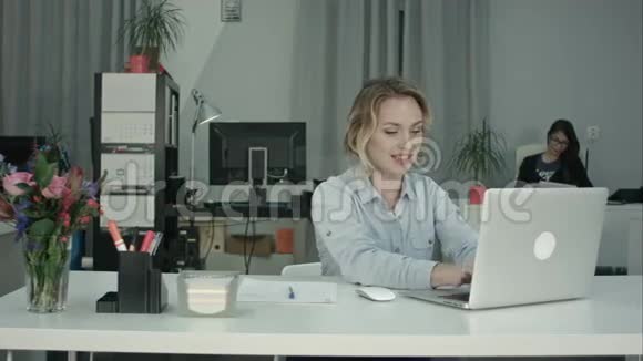 微笑的女人在笔记本电脑上打字在办公室桌上做笔记视频的预览图