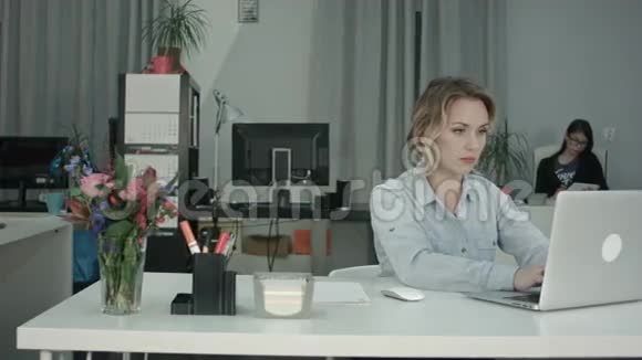工作繁忙的年轻女性在办公室的笔记本电脑上工作而她的同事在使用平板电脑视频的预览图