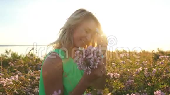 美丽的金发女郎穿着一件浅绿色的连衣裙在夕阳下采撷野花摆姿势拍照视频的预览图