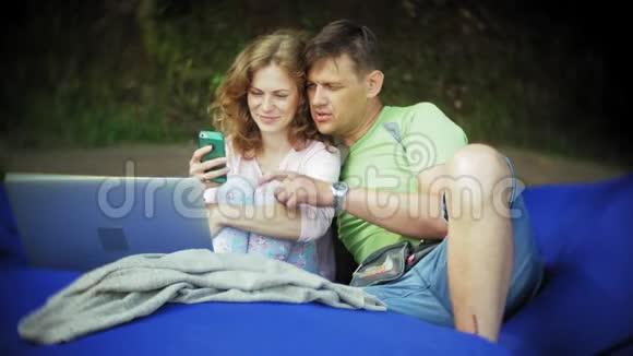 年轻女子和成熟男子使用笔记本电脑躺在公园的休息室里轻轻地吸着烟视频的预览图
