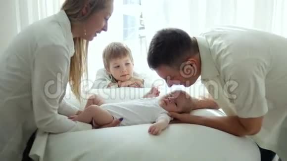 父母和父母亲吻躺在床上的新生儿视频的预览图