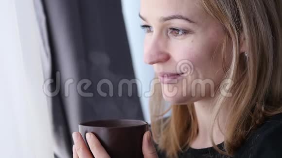 漂亮的年轻女人在窗户附近喝咖啡或茶慢动作视频的预览图