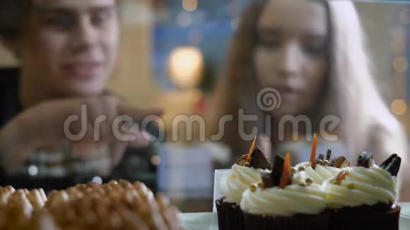 糖果店里漂亮的一对年轻人一个女孩和一个穿毛衣的男人自己选择蛋糕和甜点视频的预览图