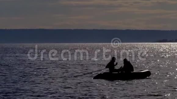 橡皮船与渔民的轮廓慢慢漂移在一个大湖上湖水在黄昏的阳光下闪耀视频的预览图