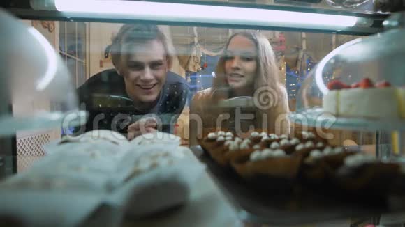 糖果店里漂亮的一对年轻人一个女孩和一个穿毛衣的男人自己选择蛋糕和甜点视频的预览图