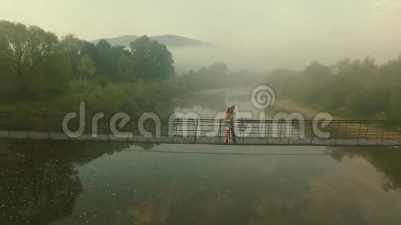 在雾中飞行摄像机在山上的木桥上鸟瞰情侣视频的预览图