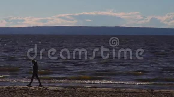 孤独一个孤独的女人慢慢地沿着一个空荡荡的沙滩沿着水边走去一个女人的轮廓视频的预览图