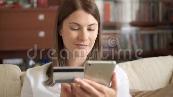 穿着白色衬衫的女人坐在客厅的沙发上用智能手机刷卡上网视频的预览图