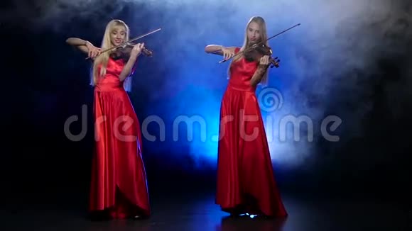 两个金发女孩拉小提琴带有背光的烟熏背景慢动作视频的预览图