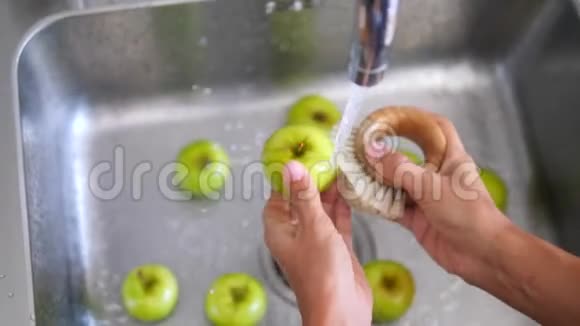 年轻的纯素女孩用竹刷洗绿苹果手拿新鲜水果在厨房水槽的自来水下视频的预览图