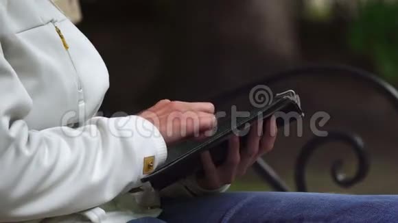 一个女人坐在公园的长凳上在平板电脑上看书她慢慢地用手指轻轻地抚摸视频的预览图