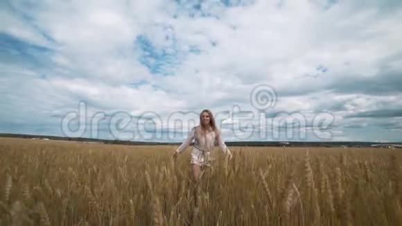 一个穿着白色连衣裙穿过麦田的美丽年轻快乐女人的完整肖像视频的预览图