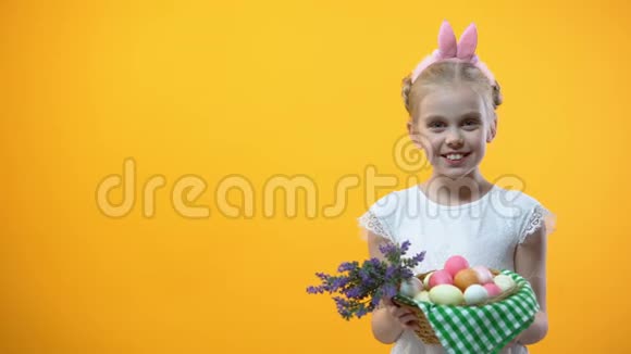 微笑的小男孩展示篮子五颜六色的鸡蛋黄色背景复活节视频的预览图